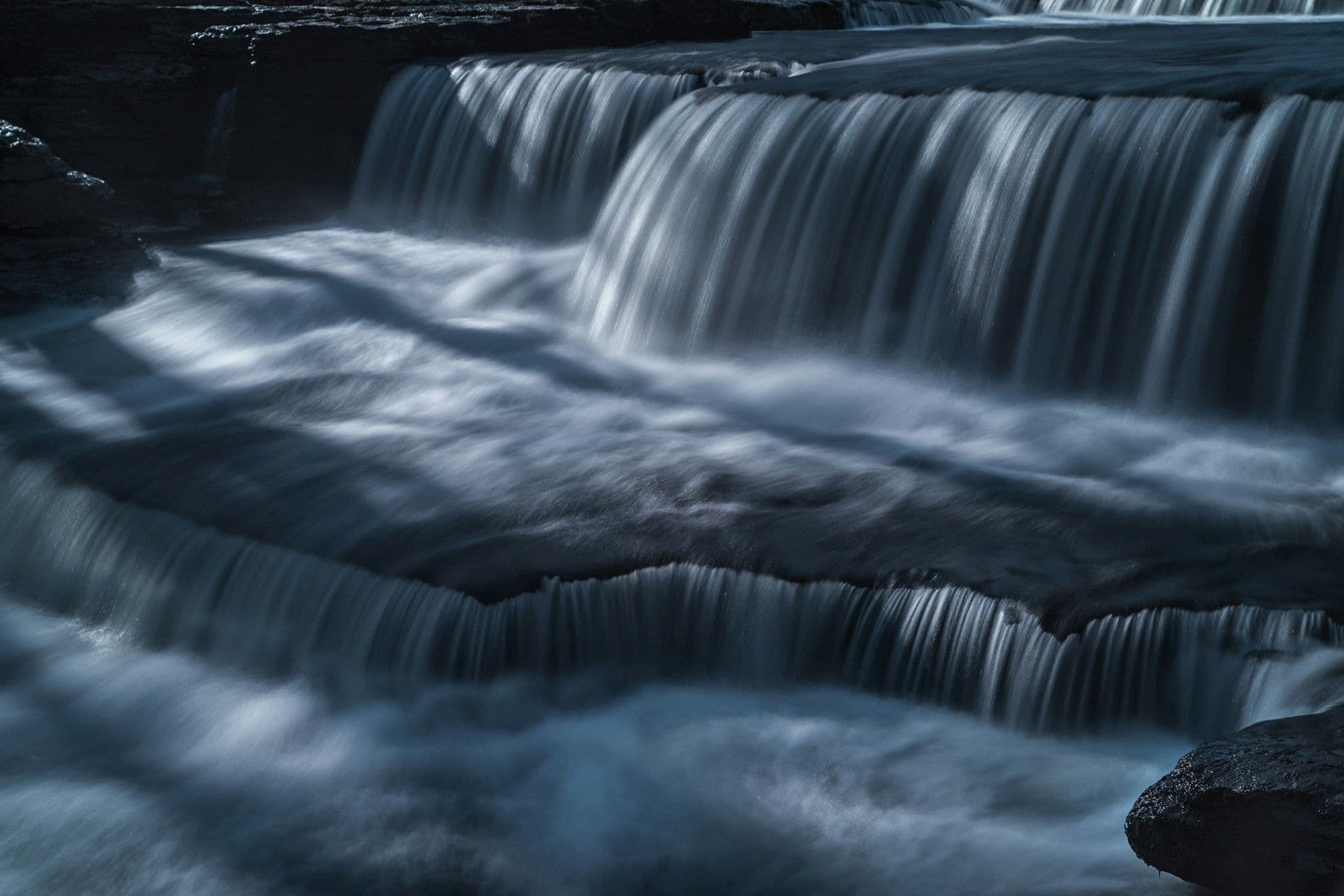 Silky white water spilling over the limestone steps of Aysgarth Lower Falls in cool evening light.