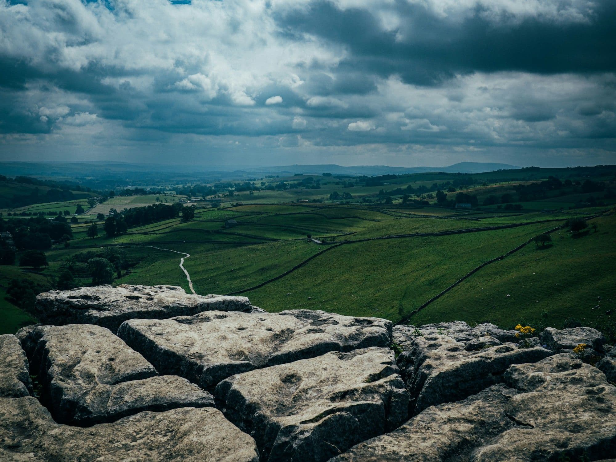 Limestone pavement at the lip of Malham Cove, the valley falling away beneath a brooding sky.